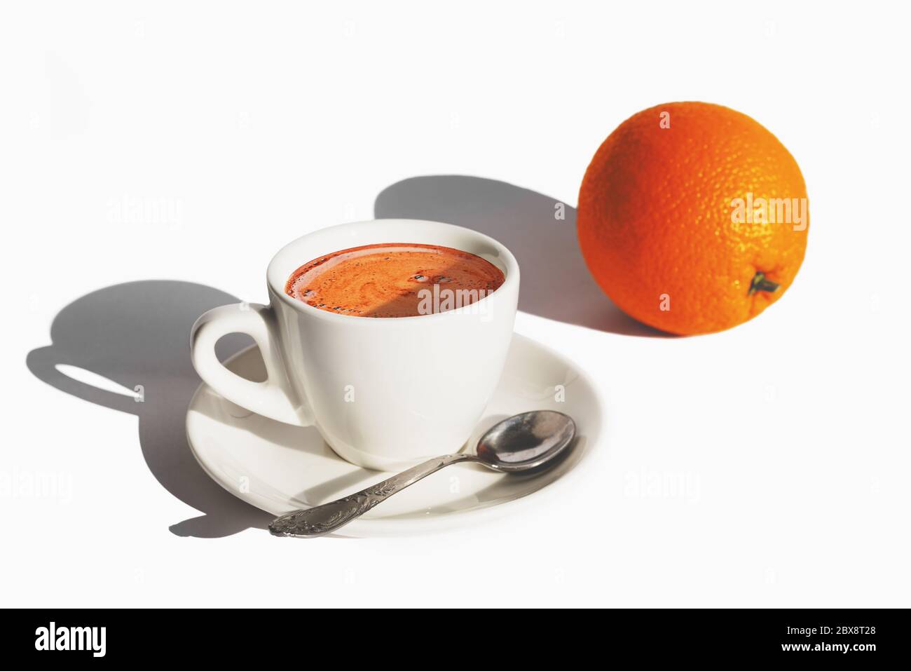 Tazza di caffè bianca e un arancio su sfondo bianco con ombre dure di luce del mattino. Il modo migliore per iniziare la giornata. Spazio di copia Foto Stock
