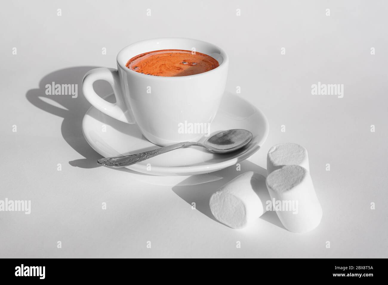 Tazza bianca di caffè su piattino e tre marshmallows con ombre dure su sfondo bianco. Stile minimalista. Tempo di caffè. Spazio di copia Foto Stock