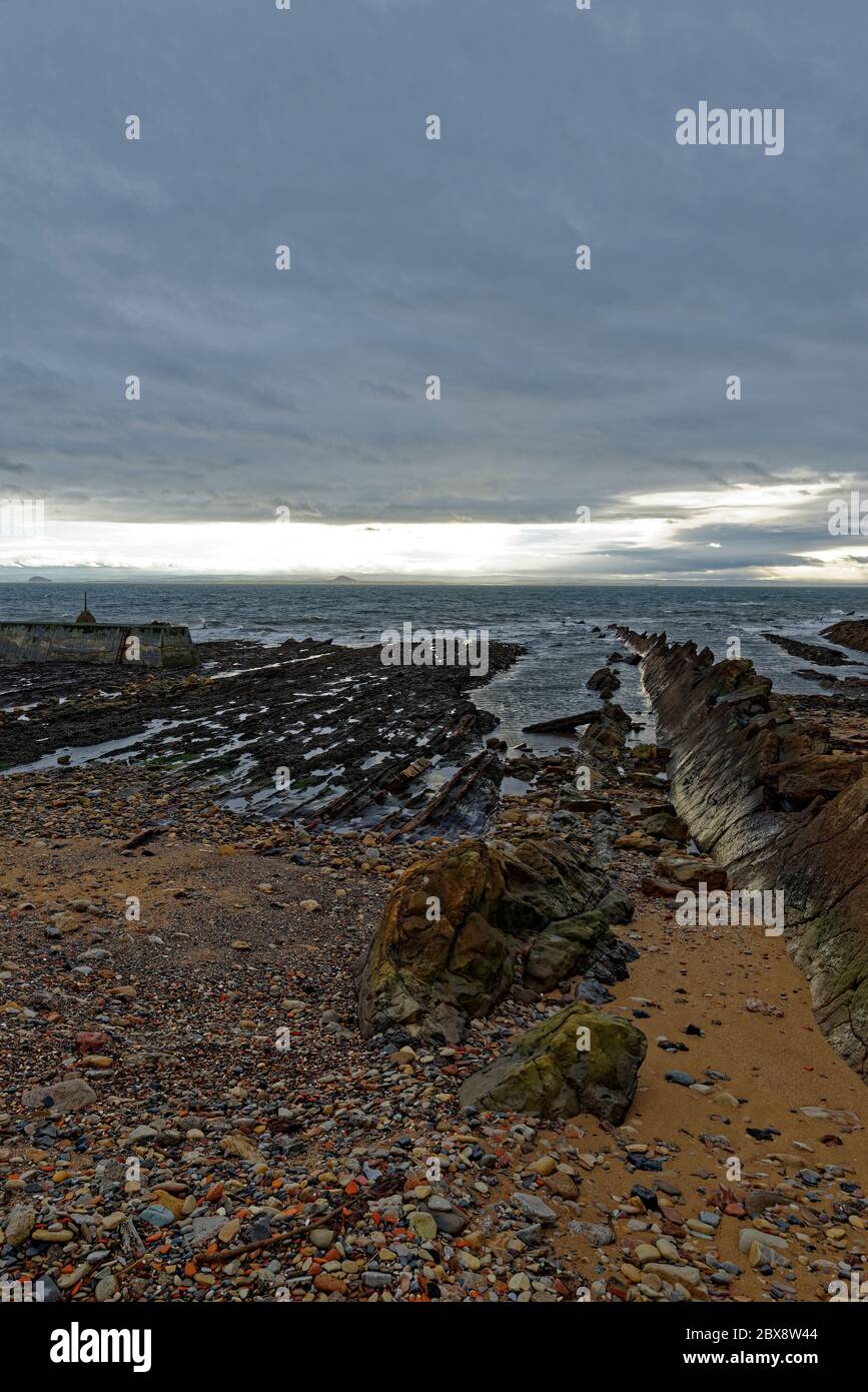 Strati di roccia che si tuffano nel mare a St Monan's sulla Costa del Fife, vicino alla Breakwater esterna del piccolo porto, con le nuvole scure invernali sopra. Foto Stock