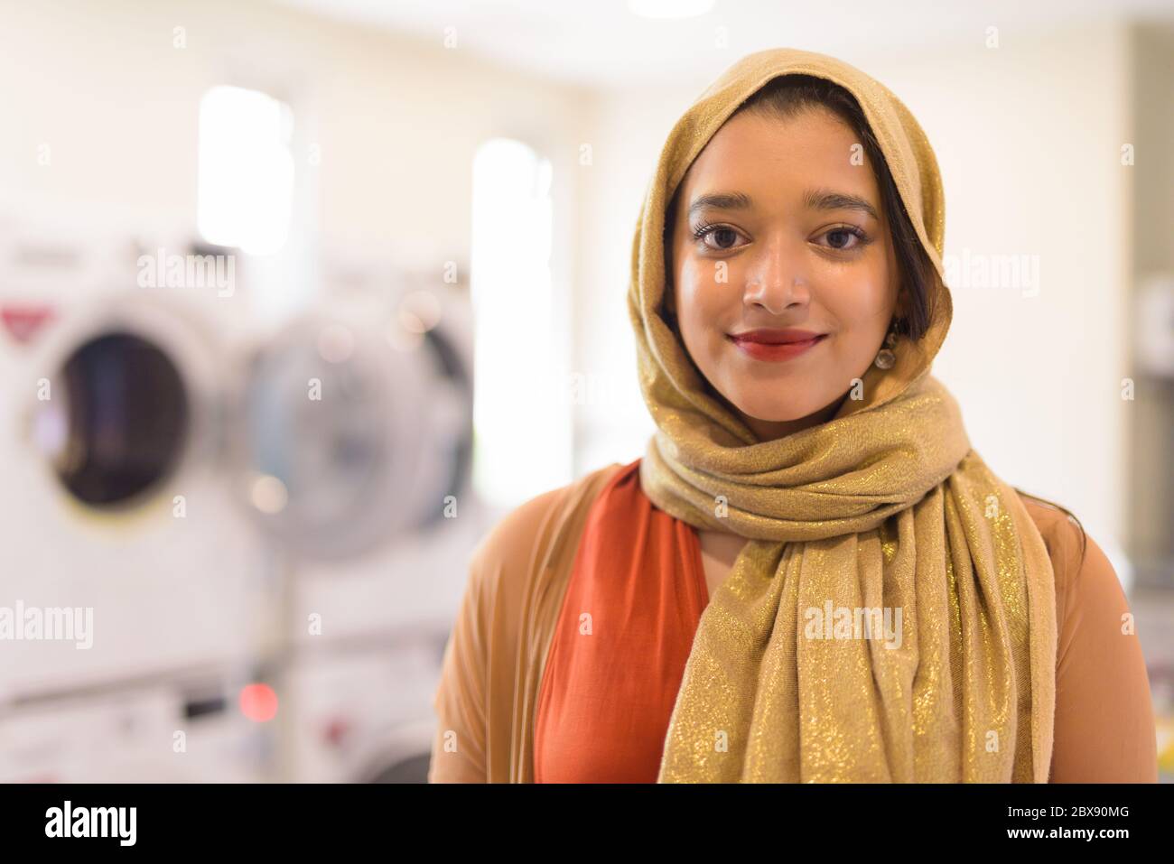 Faccia di giovane bella donna d'affari musulmana indiana come proprietario della lavanderia automatica Foto Stock