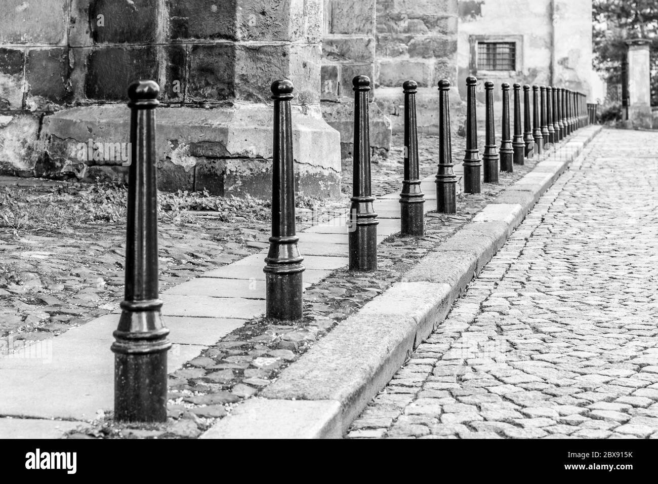 Fila di colonne di ferro tra strada acciottolata e marciapiedi pedonali. Immagine in bianco e nero. Foto Stock