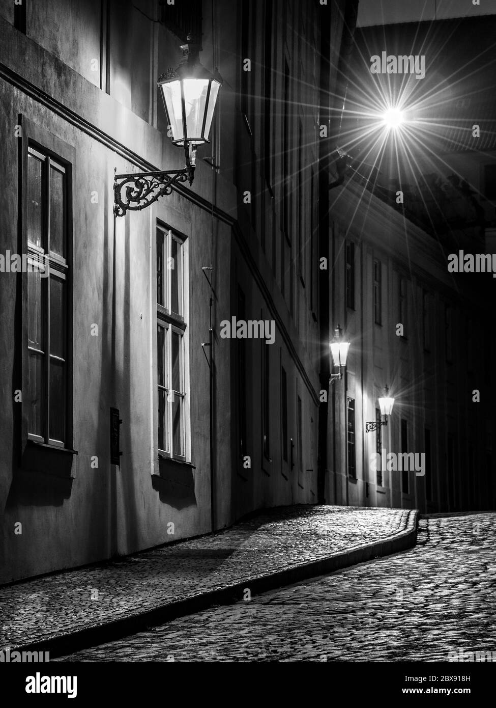 Strada acciottolata illuminata da lampioni della città vecchia, Praga, Repubblica Ceca. Immagine in bianco e nero. Foto Stock