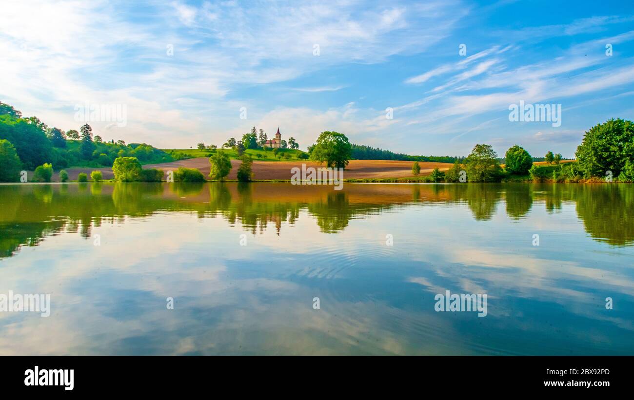 Paesaggio romantico con piccola chiesa sulla collina riflesso nello stagno. Giornata estiva soleggiata con cielo blu e nuvole bianche. San Pietro e Pauli a Bysicky vicino Lazne Belohrad, Repubblica Ceca. Foto Stock Paesaggio romantico con piccola chiesa sulla collina riflesso nello stagno. Giornata estiva soleggiata con cielo blu e nuvole bianche. San Pietro e Pauli a Bysicky vicino Lazne Belohrad, Repubblica Ceca. Foto Stock