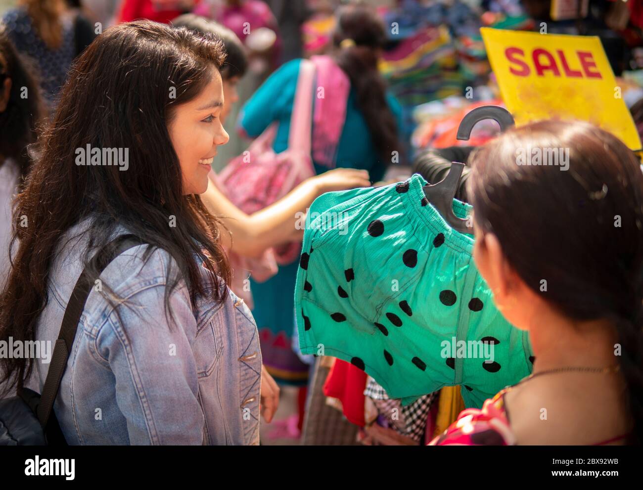 Madre felice e figlia che guardano e comprano vestiti insieme dal mercato di strada esterno di Delhi, India al giorno tempo. Foto Stock