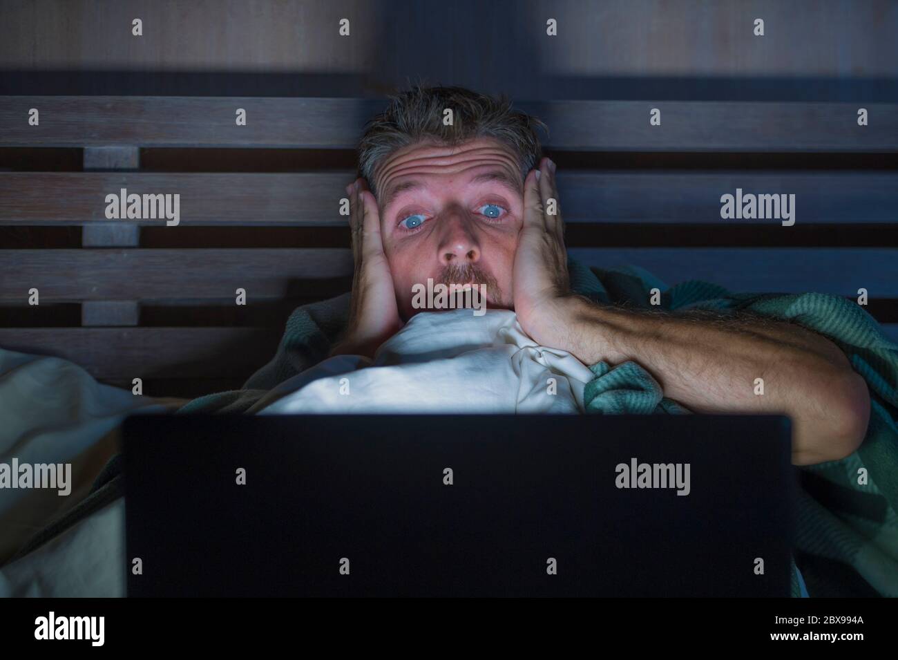 ritratto di stile di vita di giovane paura e stressato uomo a letto guardando film horror internet tarda notte con computer portatile o camera da letto tv in pa Foto Stock