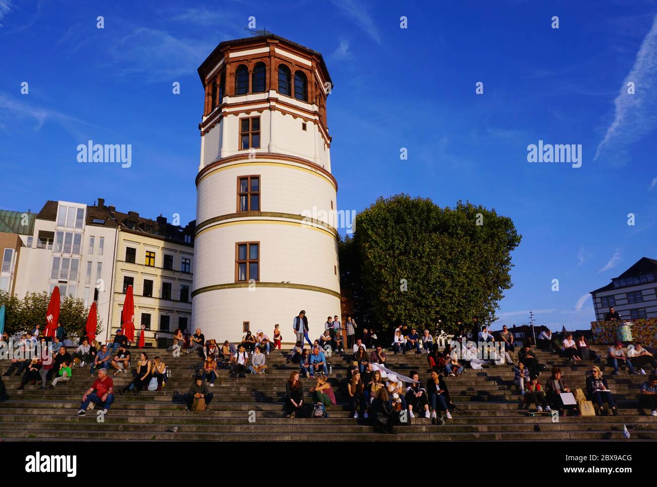 La storica „Schlossturm (torre del castello) nel centro storico di Düsseldorf con persone sedute sui gradini e godendosi il sole. Foto Stock