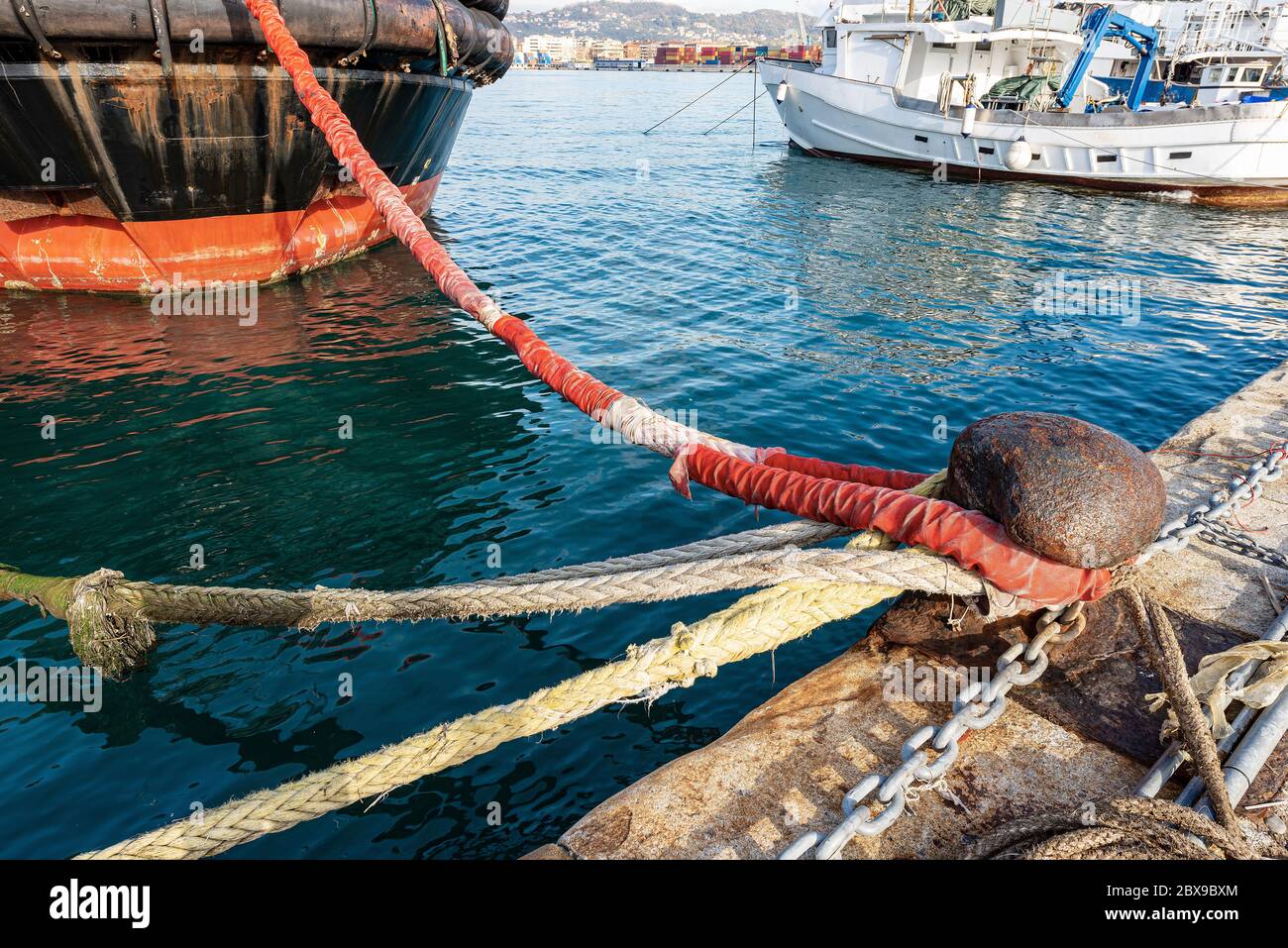 Navi ormeggiate nel porto. Grande palafitte arrugginite con falciatori, catene e corde sulla banchina del porto. La Spezia, Liguria, Italia, Europa Foto Stock