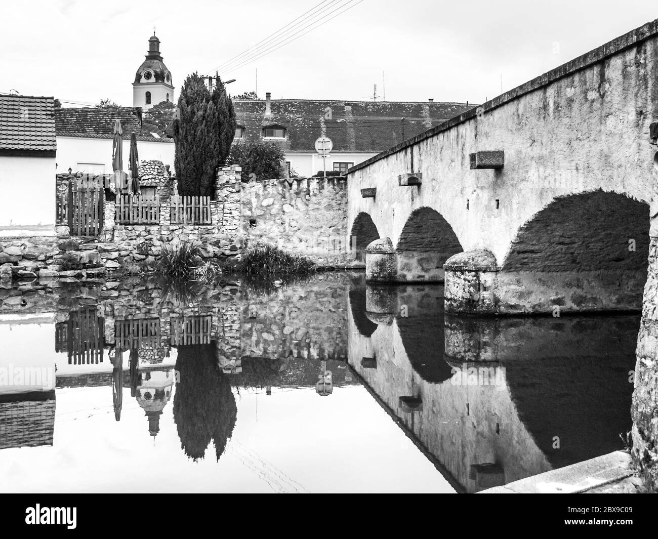 Vecchio ponte di pietra riflesso in acque calme, Putim, Boemia meridionale, Repubblica Ceca. Immagine in bianco e nero. Foto Stock