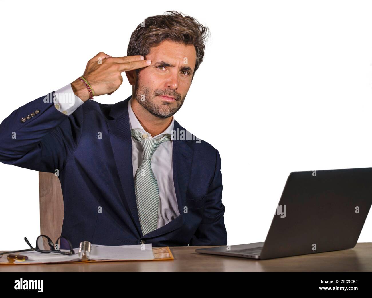 giovane uomo d'affari triste e depresso che lavora sopraffatti e frustrato sulla scrivania del computer portatile ufficio che si sente sconvolto e stressato puntando la pistola a mano fi Foto Stock