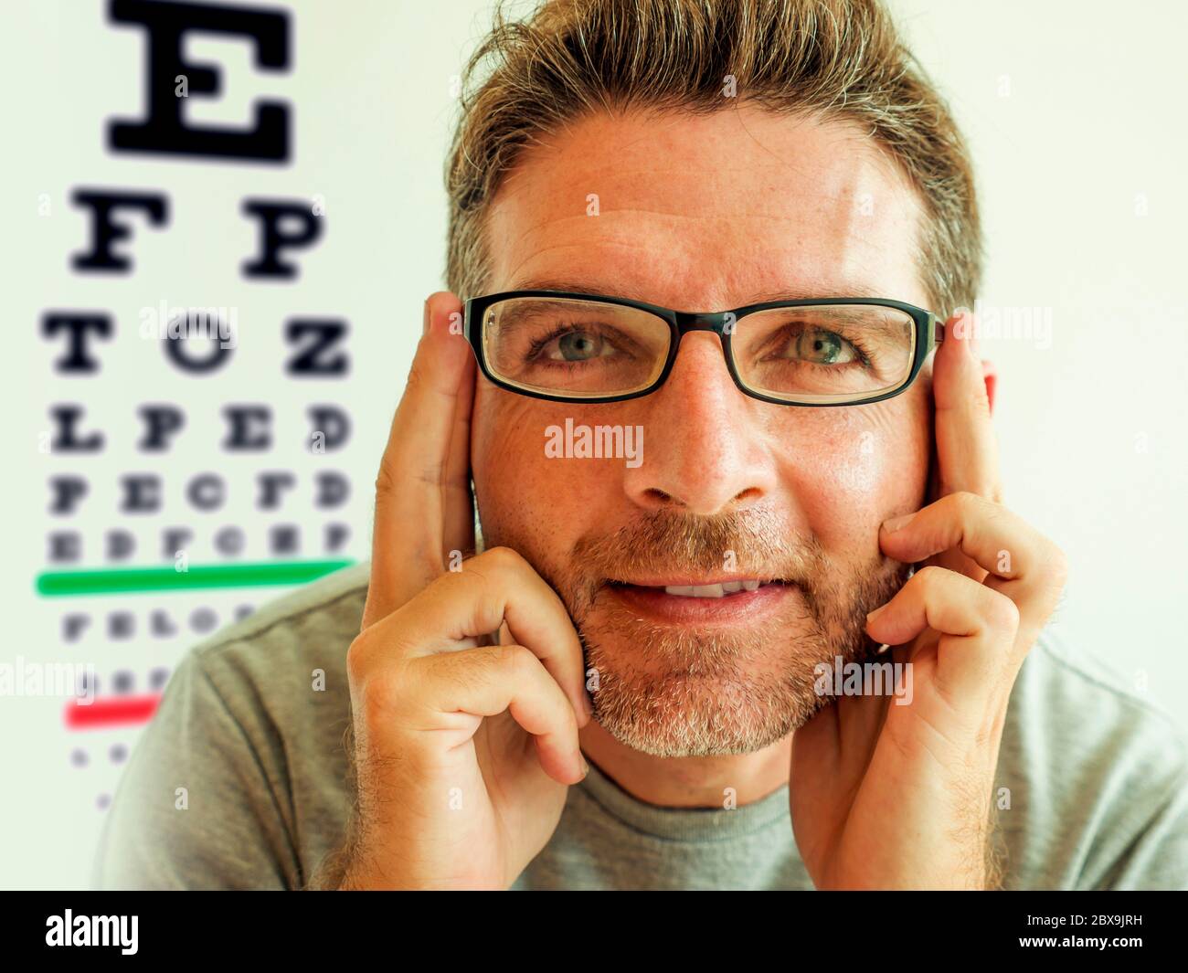 Uomo attraente che controlla la visione provando gli occhiali  all'optometrist. Allegro e bel ragazzo sui suoi 40 durante l'esame ottico  di prova occhiali per Foto stock - Alamy