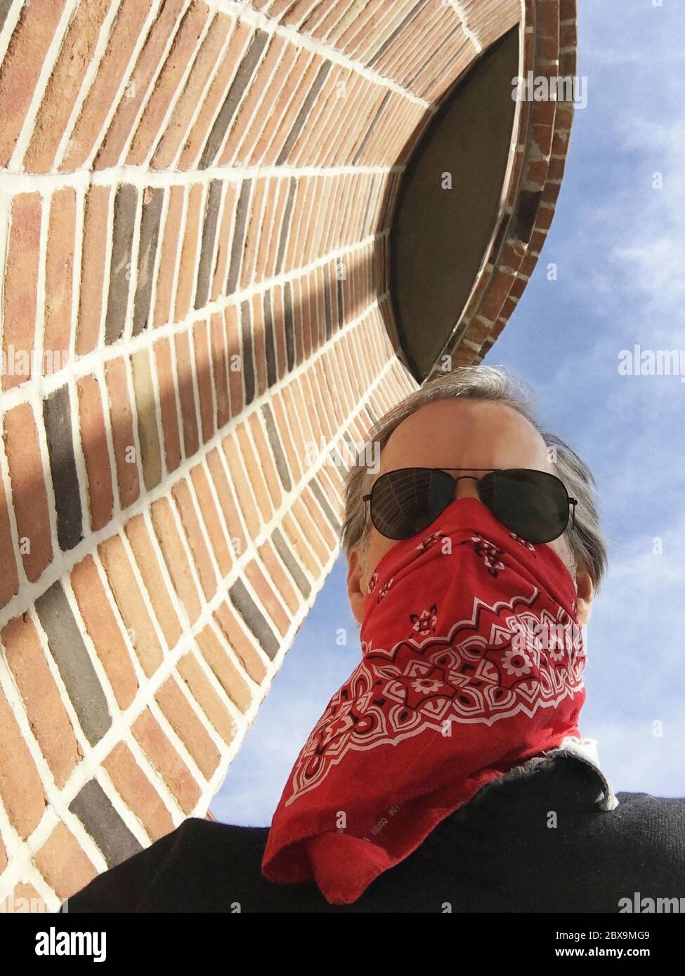 Vista ad angolo basso dell'uomo in piedi vicino alla parete di mattoni che indossa una maschera protettiva, New York City, New York, Stati Uniti Foto Stock