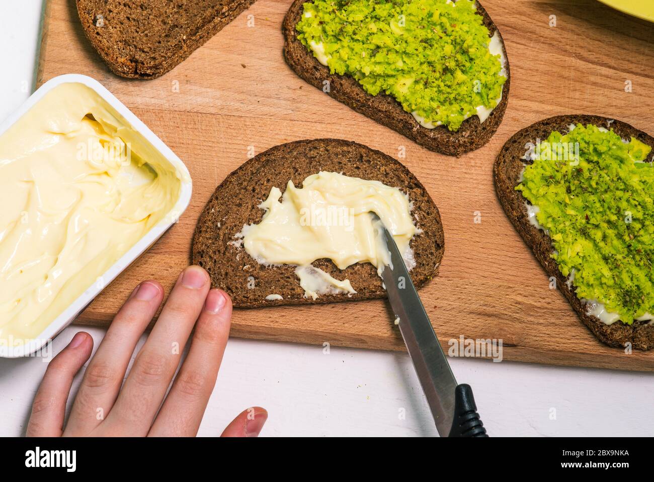 Panini all'avocado su un tavolo di legno. Il processo di preparazione di una ricetta vegetariana. Foto Stock