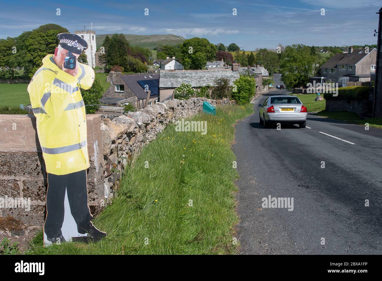 Taglio di cartone di un poliziotto che tiene una pistola ad alta velocità per aiutare il traffico lento sull'avvicinamento ad un villaggio. Cumbria, Regno Unito. Foto Stock