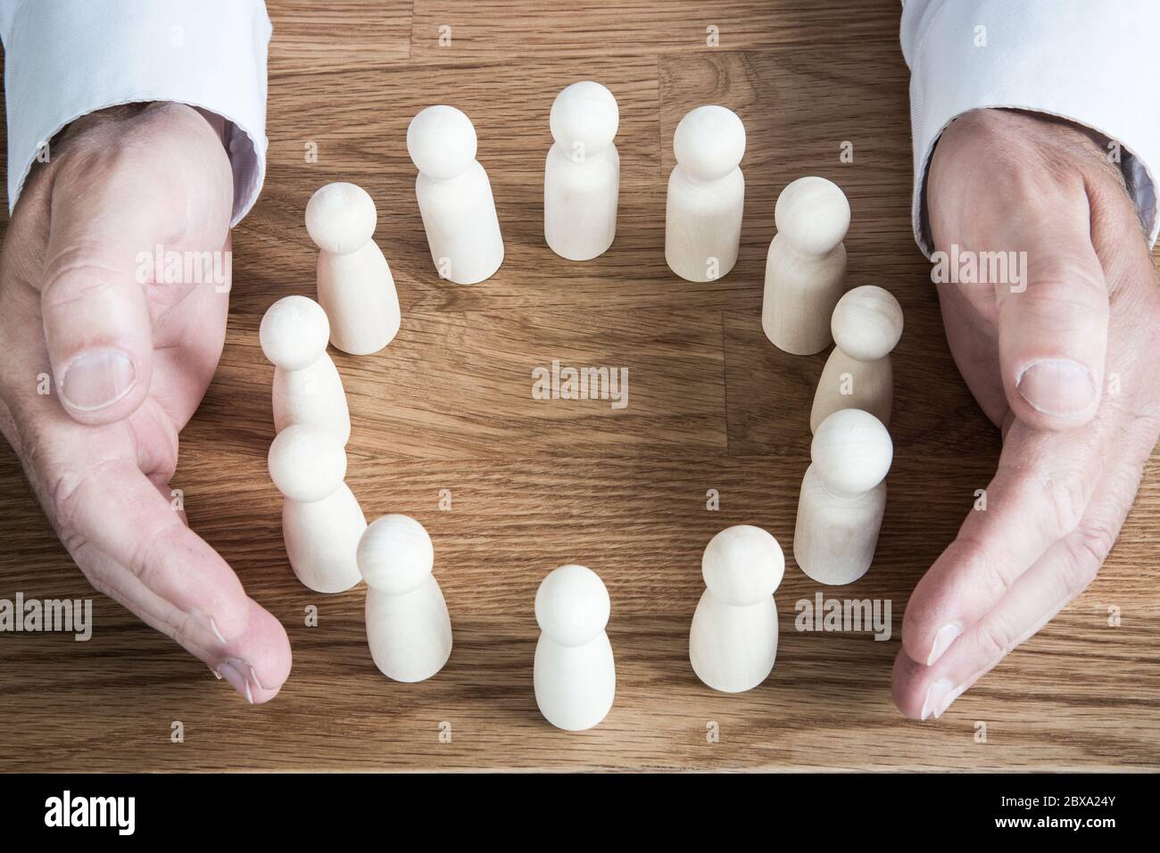 Un concetto sociale di un paio di mani umane che proteggono un gruppo di persone o dipendenti da questioni come Coronavirus, Salute mentale o professionale Foto Stock