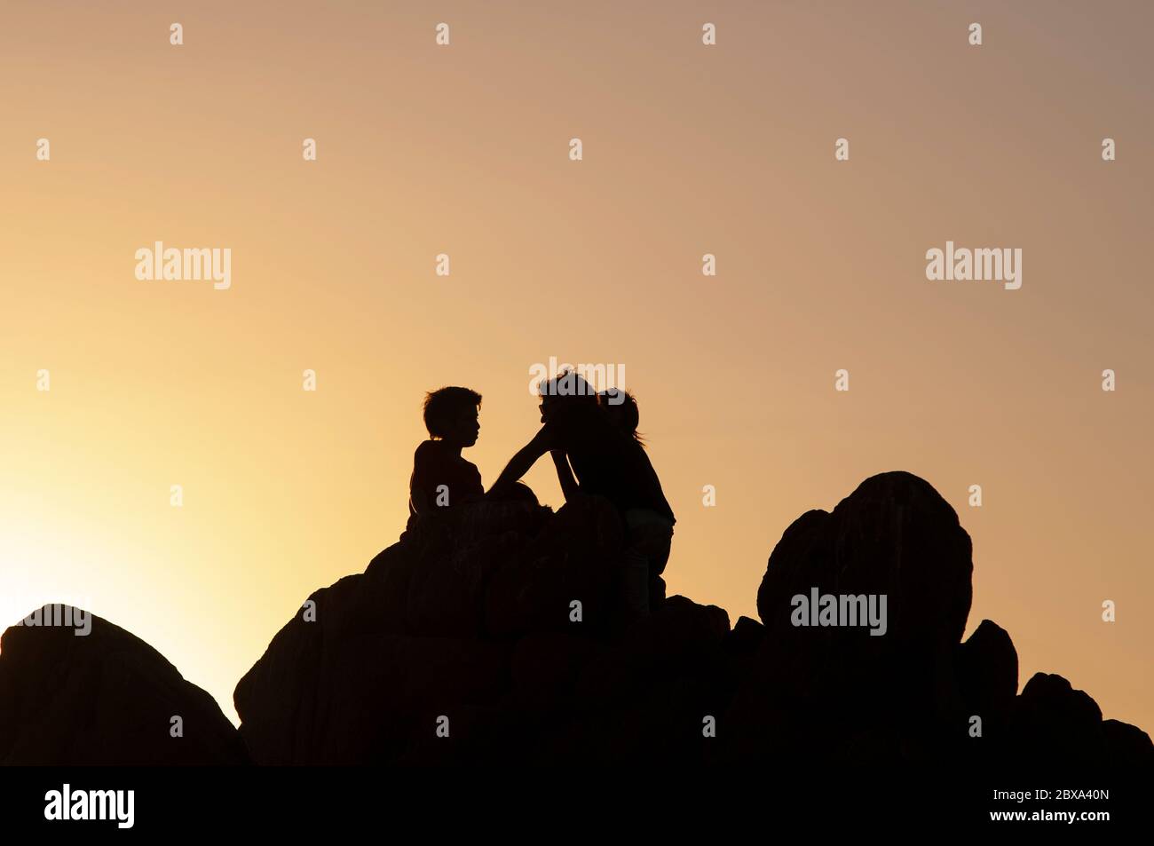 Due amici si rilassano e godono la natura sulla roccia. Silhouette di persone al tramonto sulla costa cilena Foto Stock