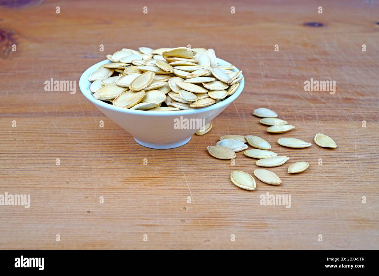 Piatto di semi di zucca organici e semi di zucca versato su sfondo di legno Foto Stock