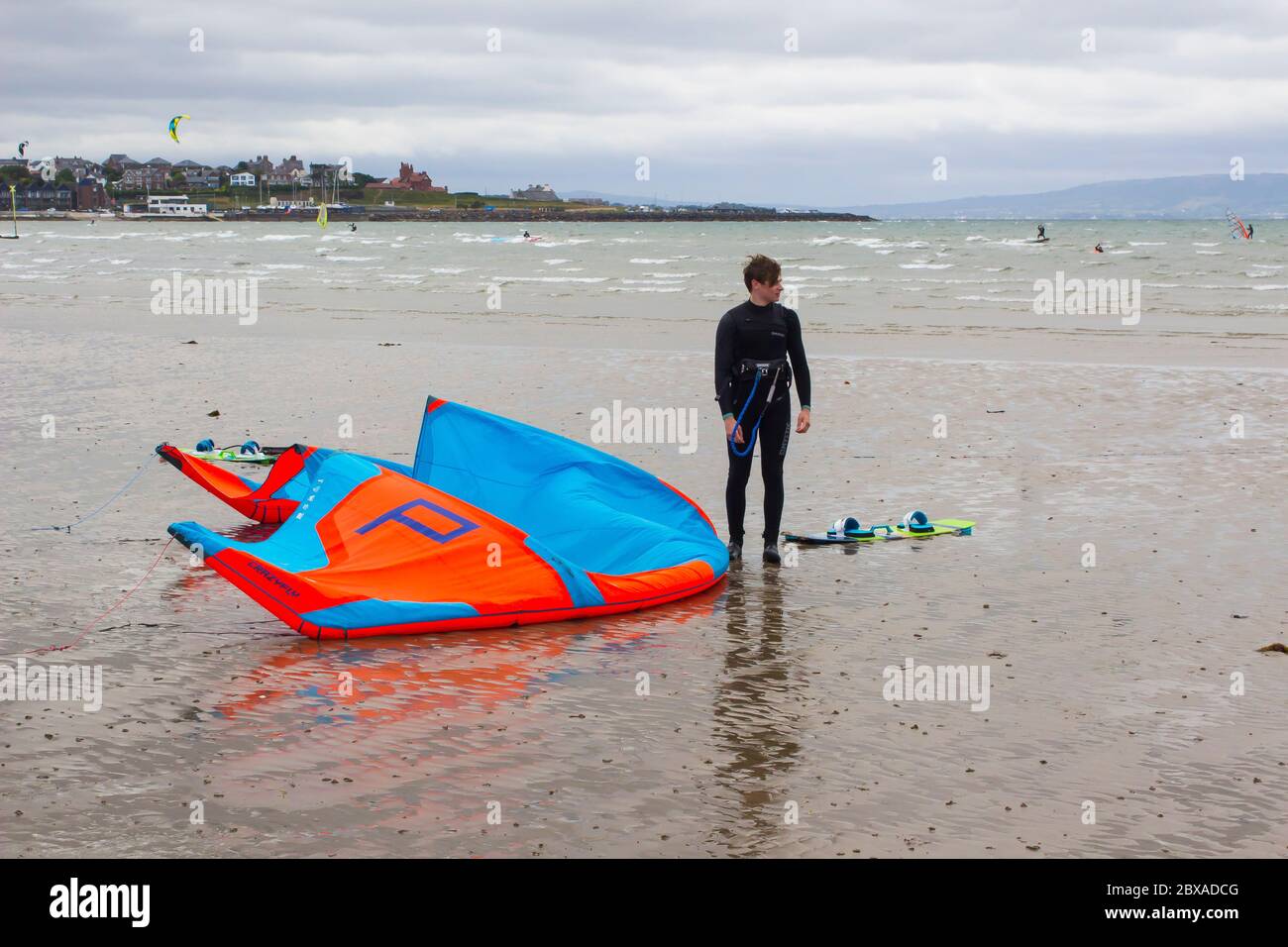 6 giugno 2020 un giorno noioso e un giovane kite maschile surfer prende un riposo di benvenuto accanto alla sua attrezzatura al bordo dell'acqua sulla spiaggia di Ballyholme a Bangor, Nord Foto Stock