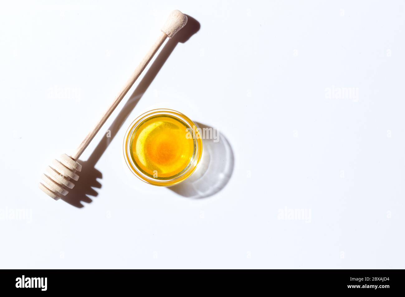 Miele in un piccolo piatto di vetro su sfondo bianco. Nelle vicinanze si trova un cucchiaio di legno Foto Stock