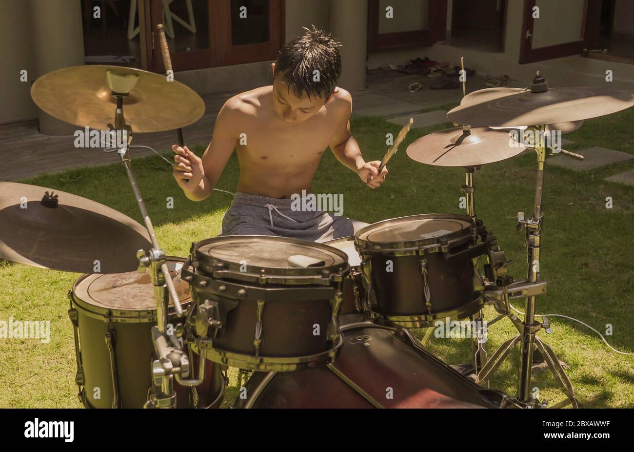 Teenager asiatico americano che gioca dums. Ritratto estivo di bel ragazzo che pratica su drum kit a casa giardino prova rock canzone provando il suo ho Foto Stock