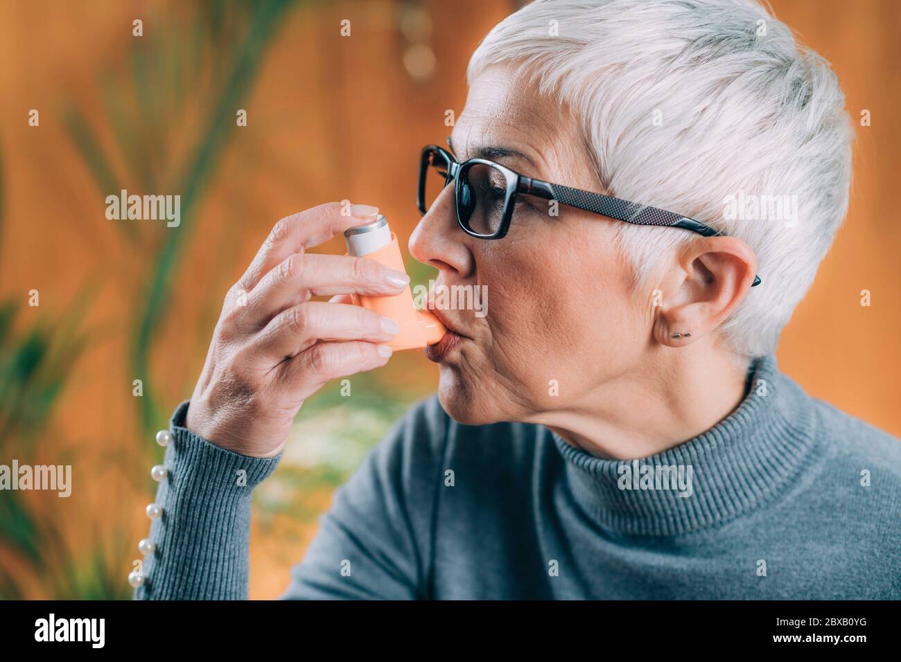 Donna anziana che usa l'inalatore per asma con tubo di prolunga Foto Stock