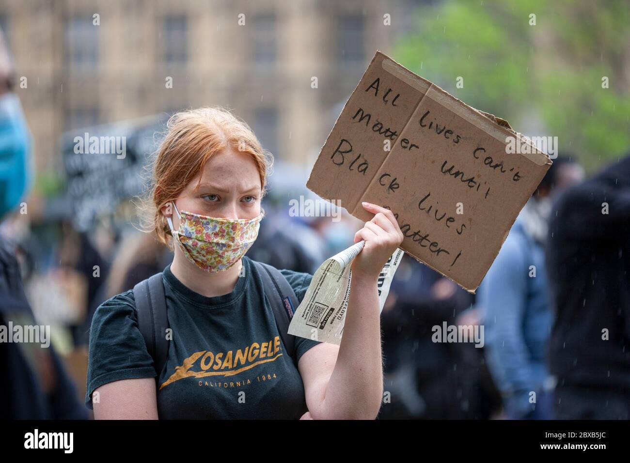 Giovane donna, indossando una maschera facciale e una T-shirt Los Angeles, tenere un cartello fatto in casa, alla protesta Black Lives Matter UK, Parliament Square, Londra UK Foto Stock