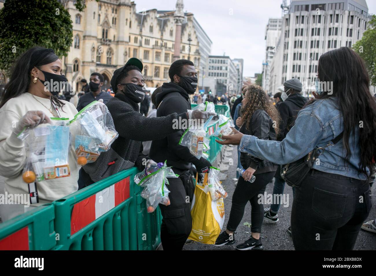 Un gruppo di giovani volontari dà gratuitamente sacchetti con una maschera, disinfettante, clementina e succo ai dimostranti al raduno anti-razzismo nel centro di Londra. Foto Stock