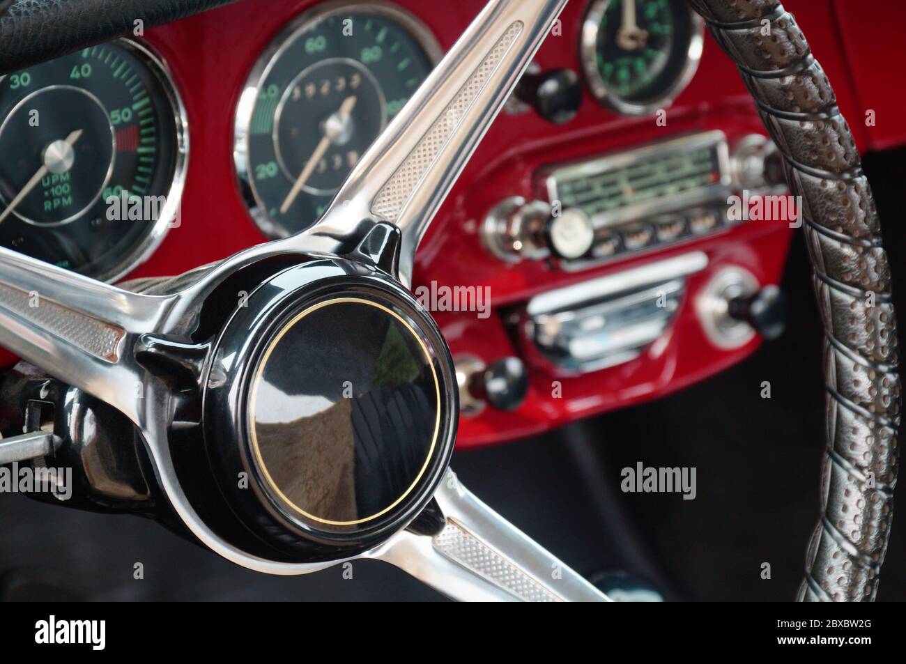 Volante, tachimetro, giri, quadranti dell'orologio, bilancia radio, pulsanti e manopole sul pannello anteriore rosso coupé vecchia vettura sportiva timer Foto Stock