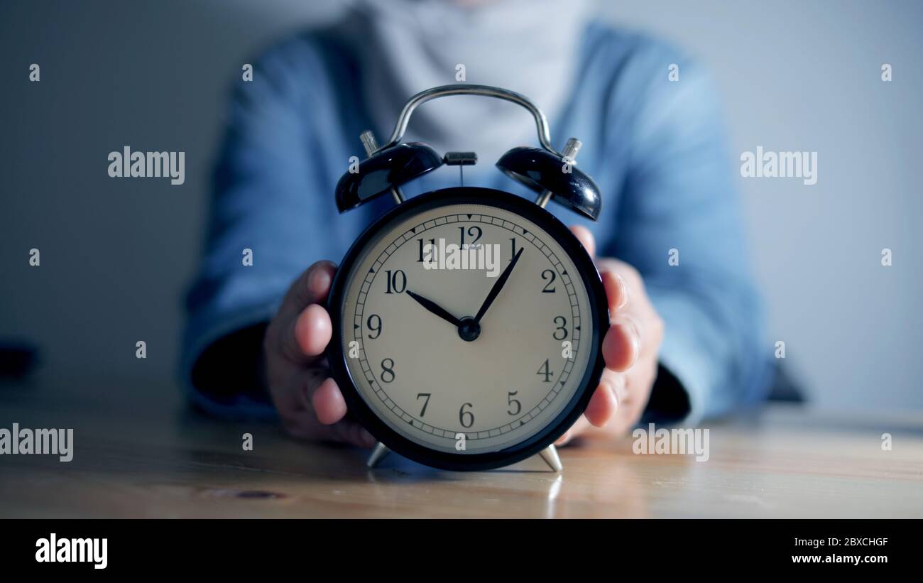 Donna che tiene sveglia, concetto di gestione del tempo, fuoco selettivo sull'orologio con la persona sfocata Foto Stock