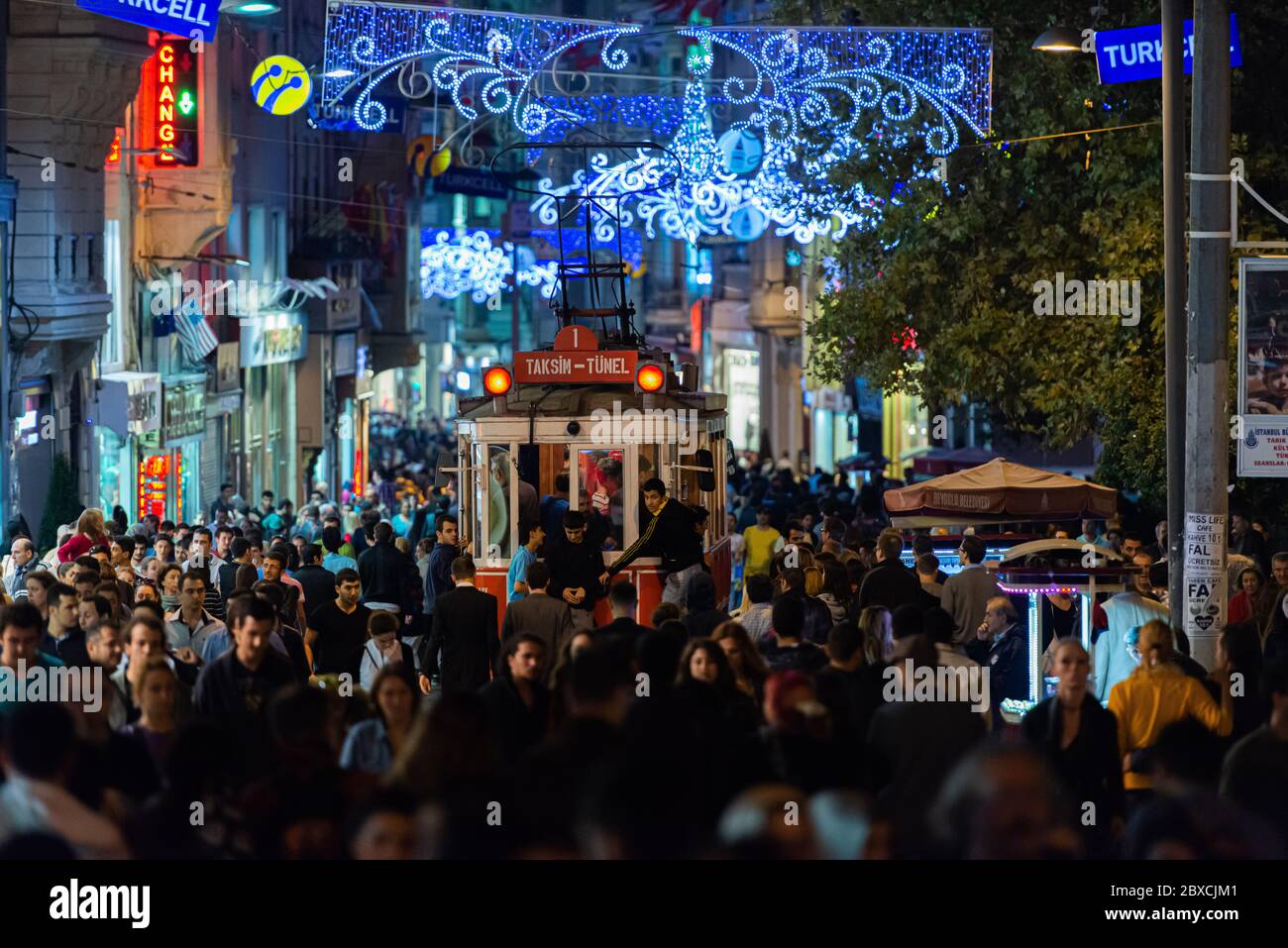 Una strada affollata di notte con lo storico tram rosso che passa nel mezzo della folla di Istanbul, Turchia Foto Stock