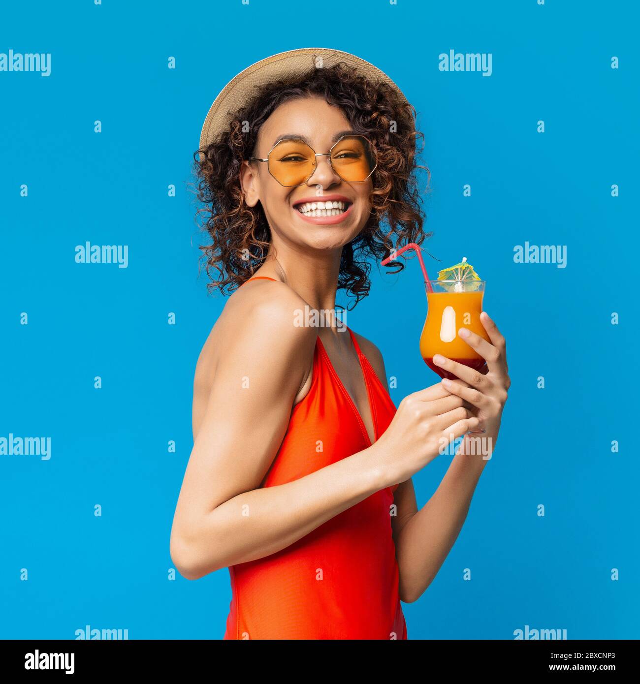 Drink estivo. Donna africana positiva gustando un cocktail di frutta colorato su sfondo blu Foto Stock