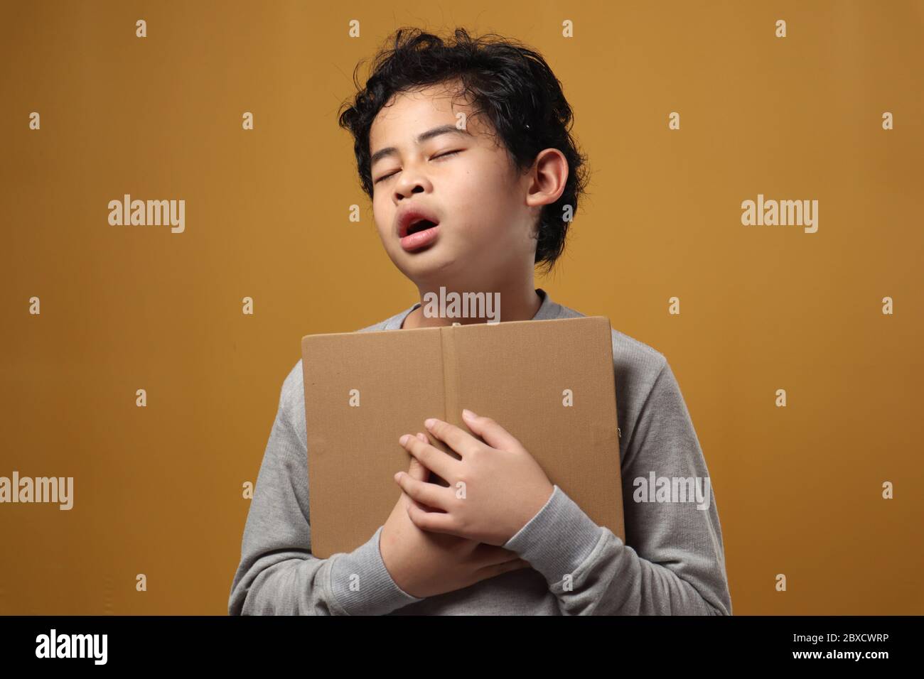 Ritratto di giovane studente asiatico ragazzo stanco dormì durante la lettura di un libro, studente stanco quando studiava duro, su sfondo giallo Foto Stock
