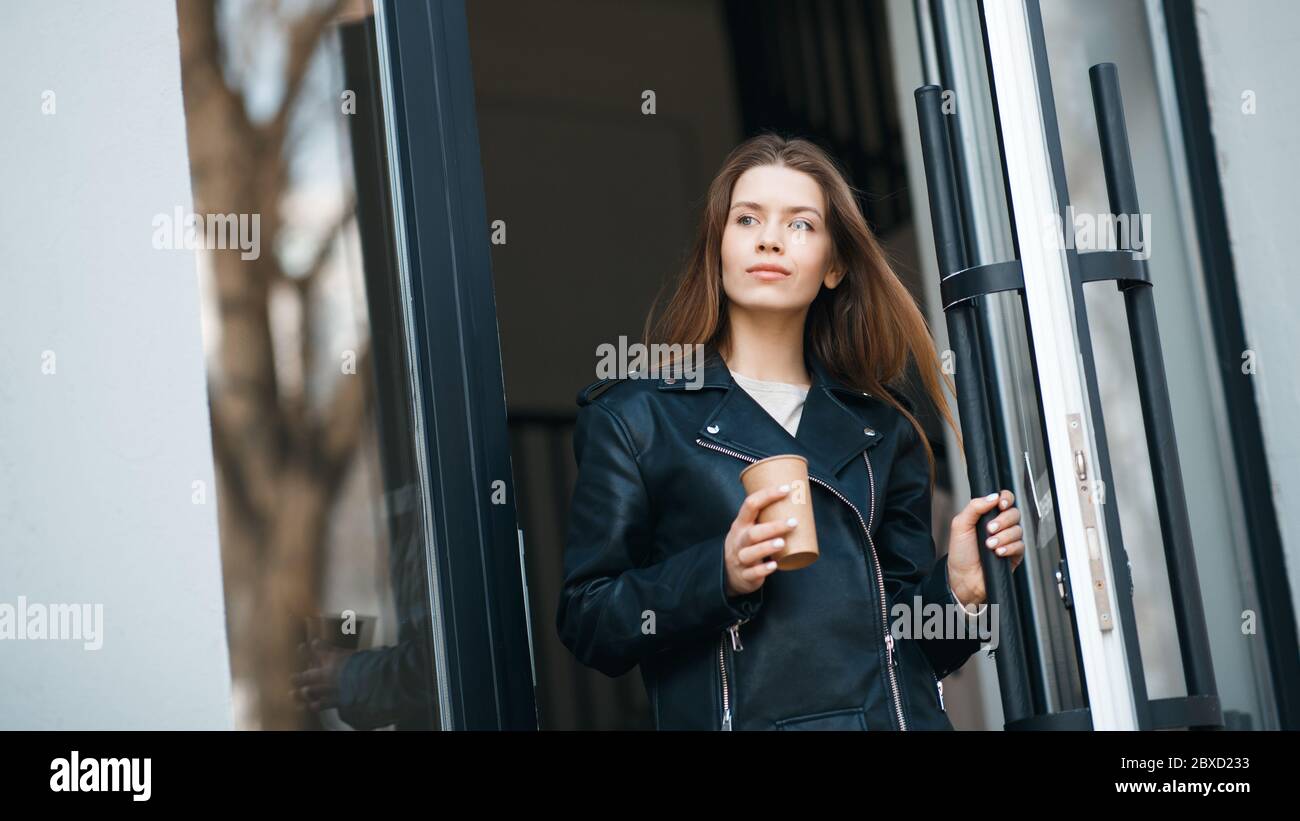Giovane donna che esce dall'edificio urbano attraverso una grande porta di vetro Foto Stock