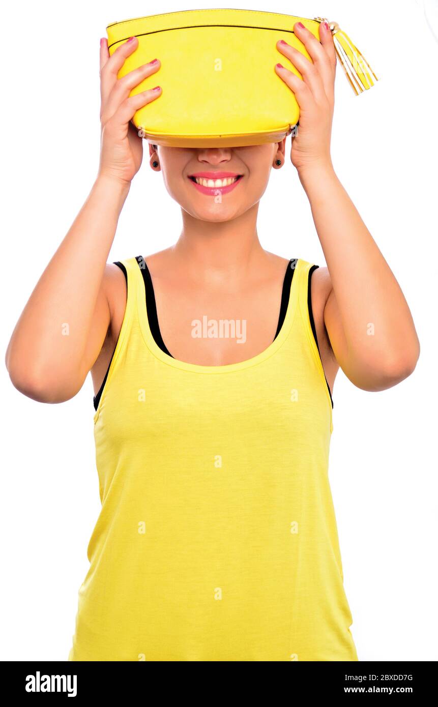Ragazza che indossa una t-shirt gialla e orecchini che tengono una borsetta gialla sopra i suoi occhi, con un bel sorriso in uno studio fotografico su uno sfondo bianco Foto Stock