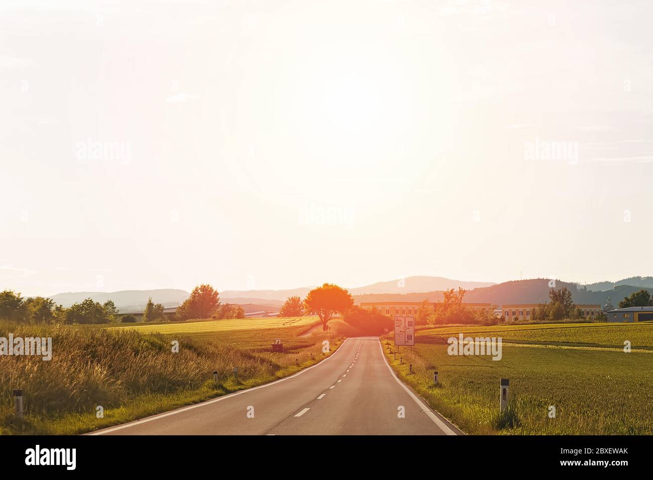 Piccola strada di campagna europea attraverso campi con colline sullo sfondo e luce calda. . Foto Stock