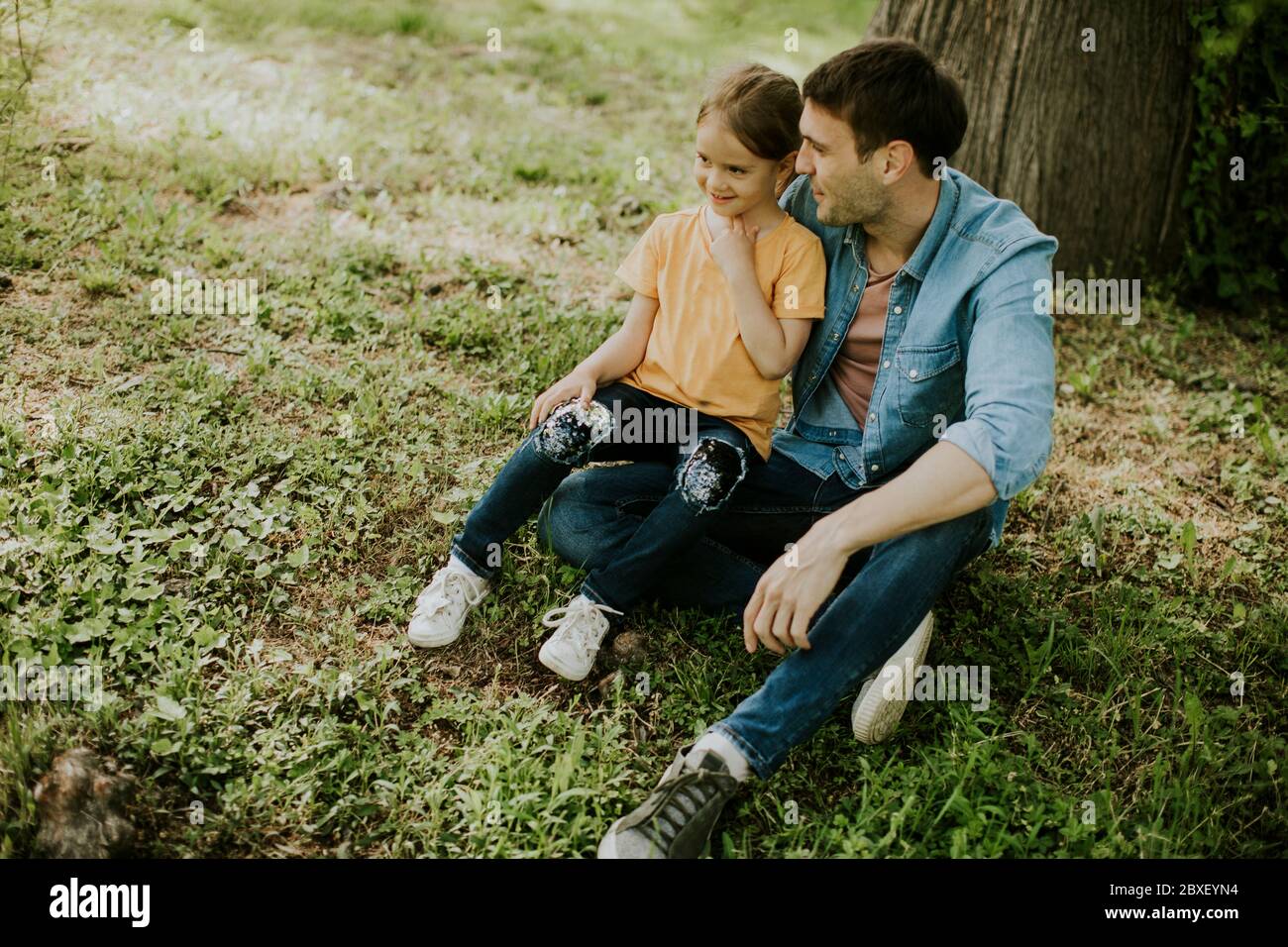 Un solo padre seduto sull'erba dall'albero con la piccola figlia carina Foto Stock