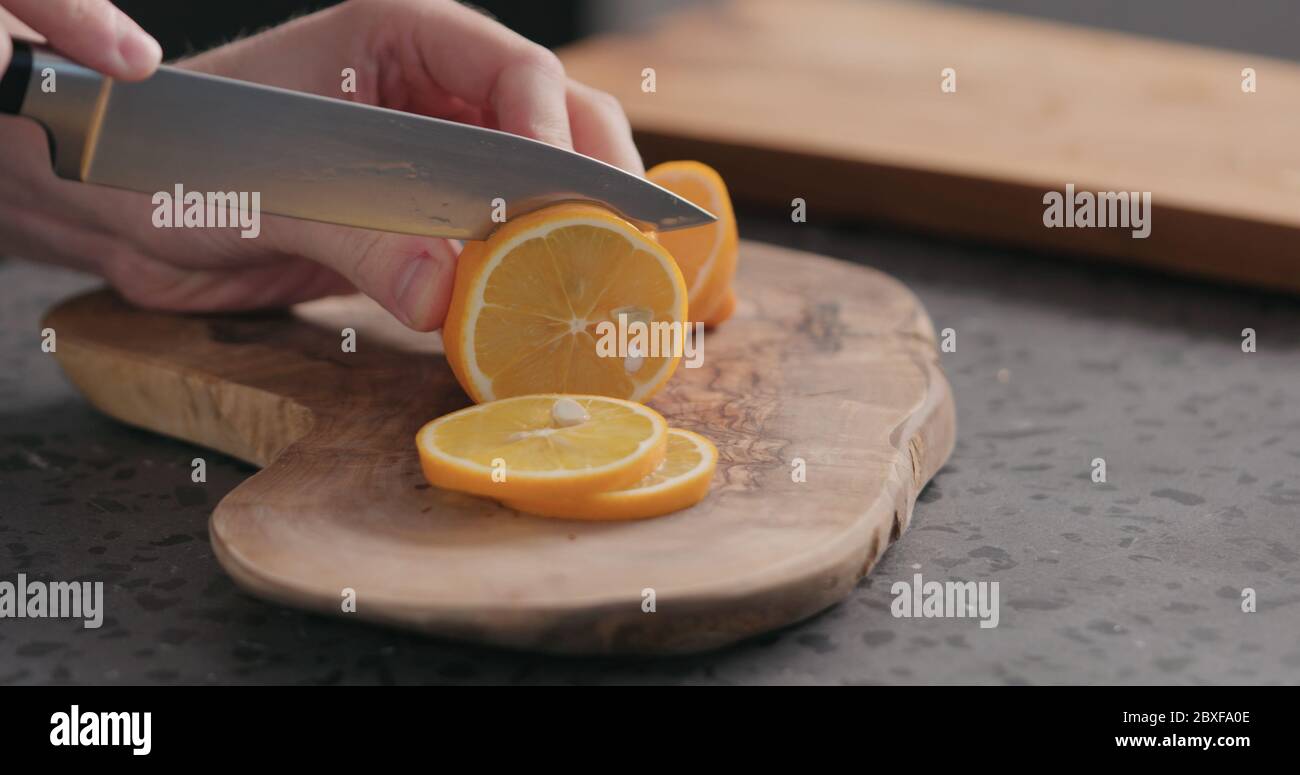 uomo che affetta limone d'arancia fresco su tavola d'oliva Foto Stock