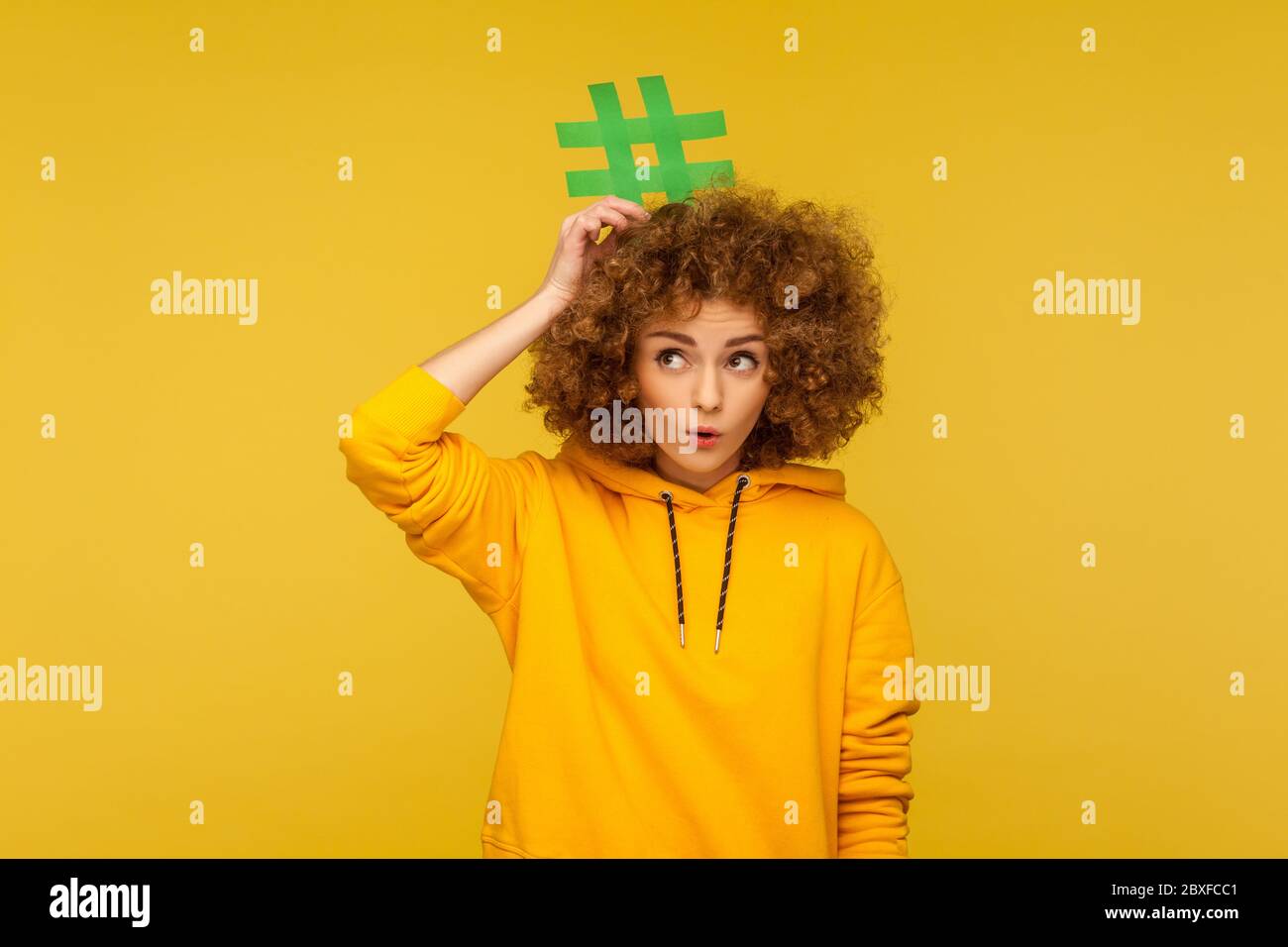 Post popolari del blog, contenuti alla moda. Ritratto di donna con capelli ricci sorpresi in stile urbano felpa con cappuccio che tiene il segno hashtag sulla testa, guardando con stupore Foto Stock