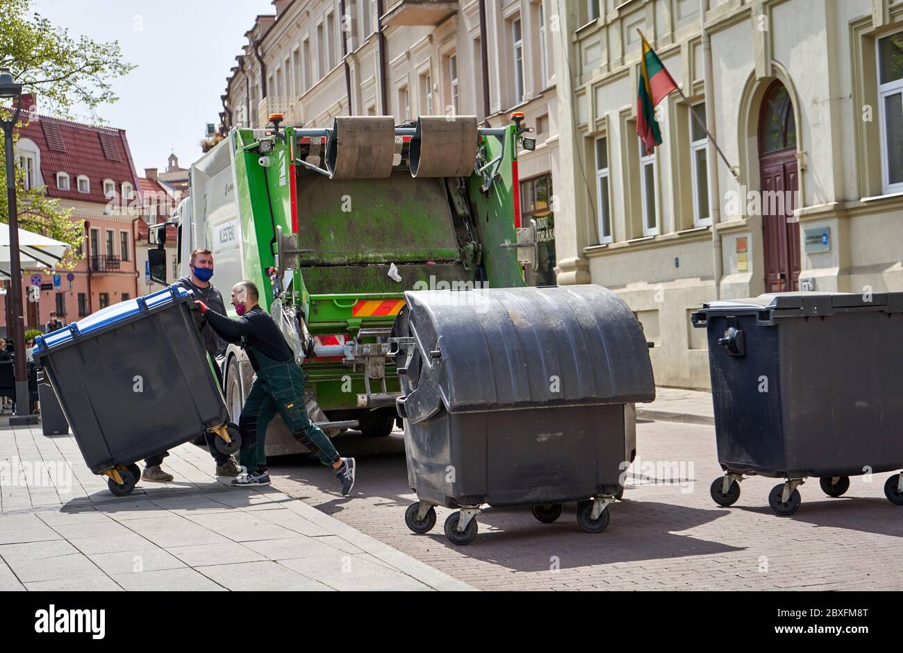 I lavoratori che svuotano i bidoni dei rifiuti per il camion dei rifiuti in strada Foto Stock