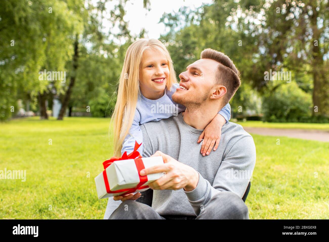 Il giorno del Padre. Felice figlia di famiglia che abbracciano papà e ride in vacanza. La ragazza ha dato un regalo al papà nel parco Foto Stock