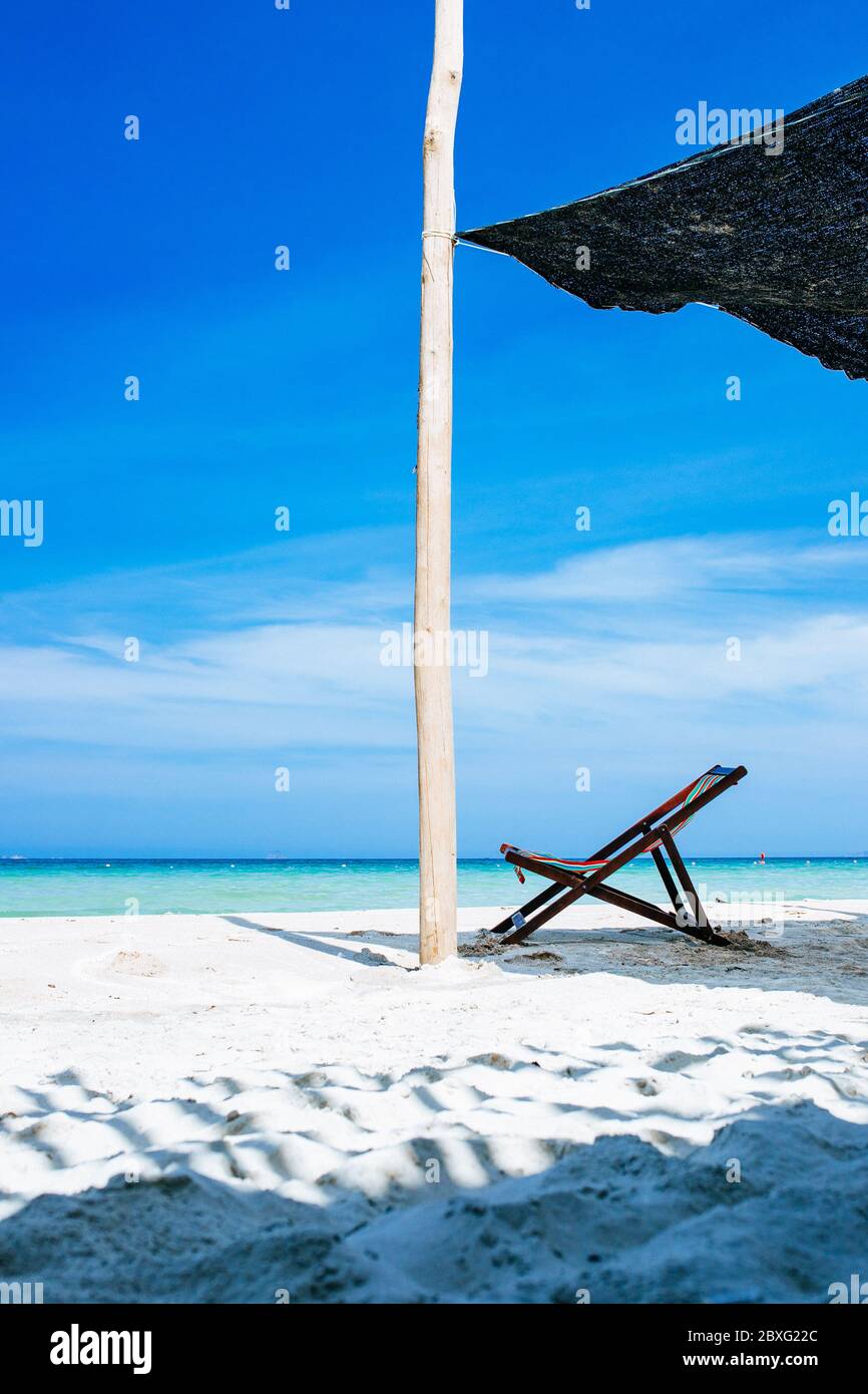 Una sedia a sdraio è all'ombra sull'oceano, senza persone. Con un cielo blu con nuvole bianche sullo sfondo. Un luogo di relax e riposo sul th Foto Stock