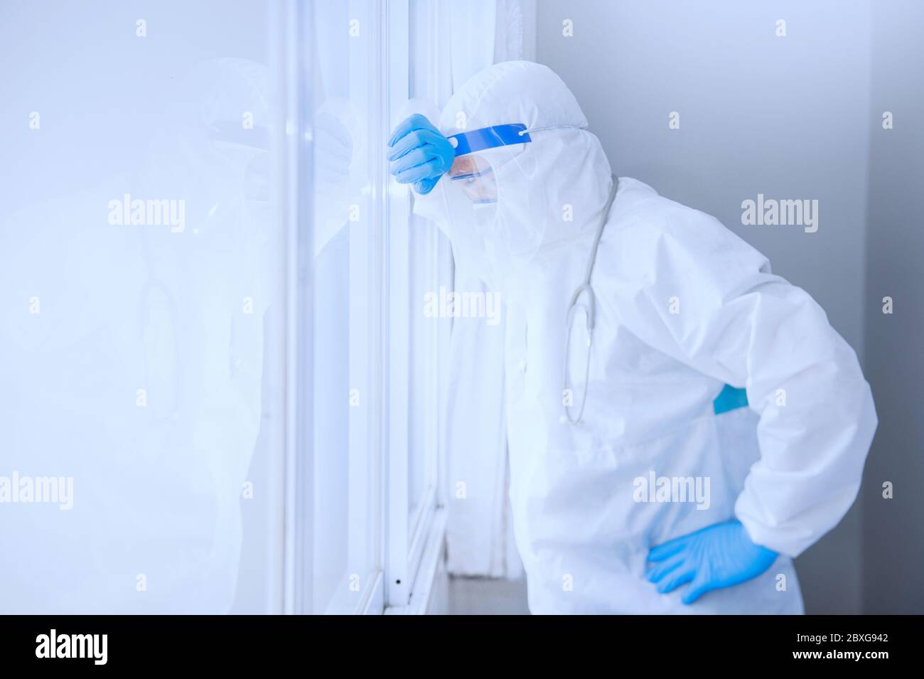 Medico stanco che indossa i DPI appoggiati contro una finestra, Thailandia Foto Stock