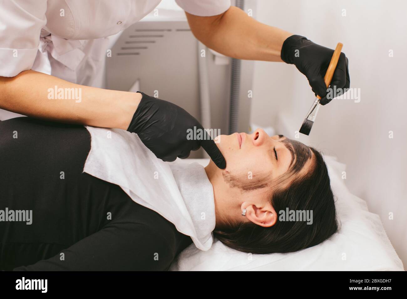 Estetista preparando una donna per un trattamento di bellezza con buccia di carbonio in una clinica Foto Stock