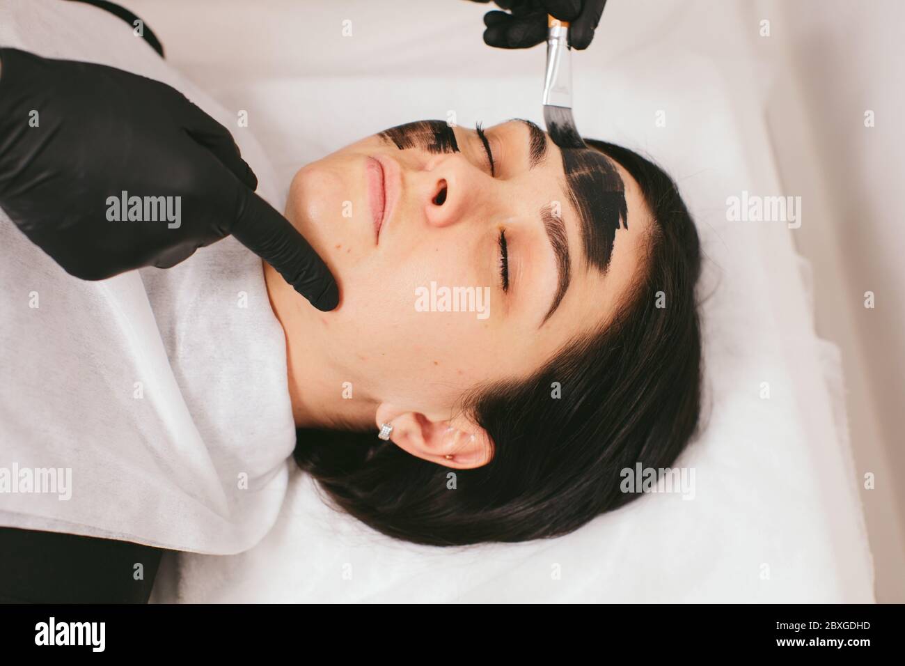 Estetista preparando una donna per un trattamento di bellezza con buccia di carbonio in una clinica Foto Stock