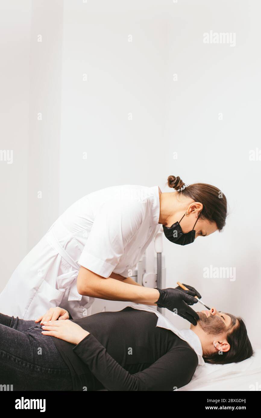 Estetista preparando una donna per un trattamento di bellezza con buccia di carbonio in una clinica Foto Stock