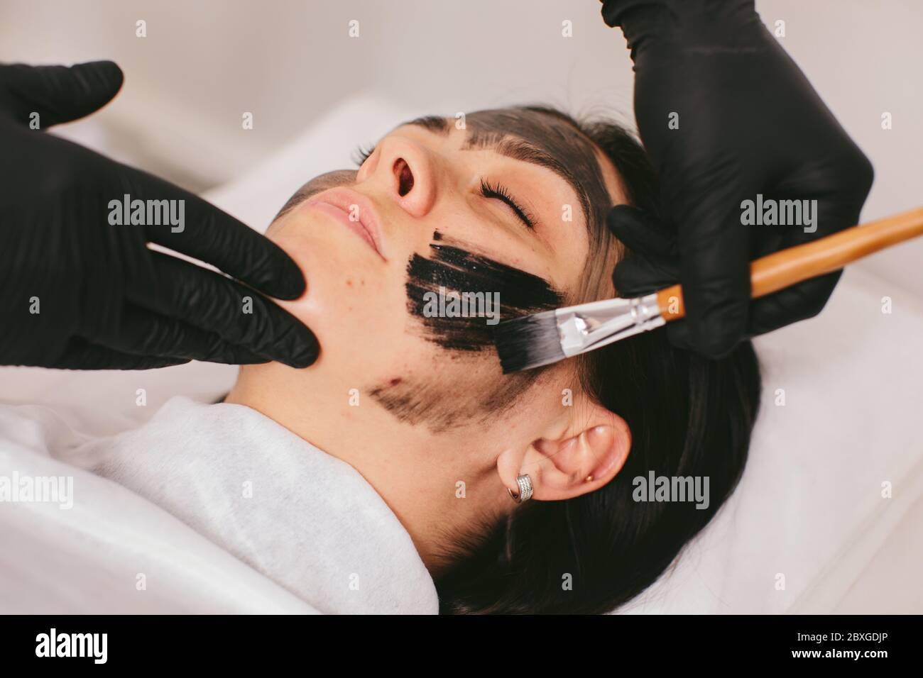 Estetista preparando una donna per un trattamento di bellezza con buccia di carbonio in una clinica Foto Stock