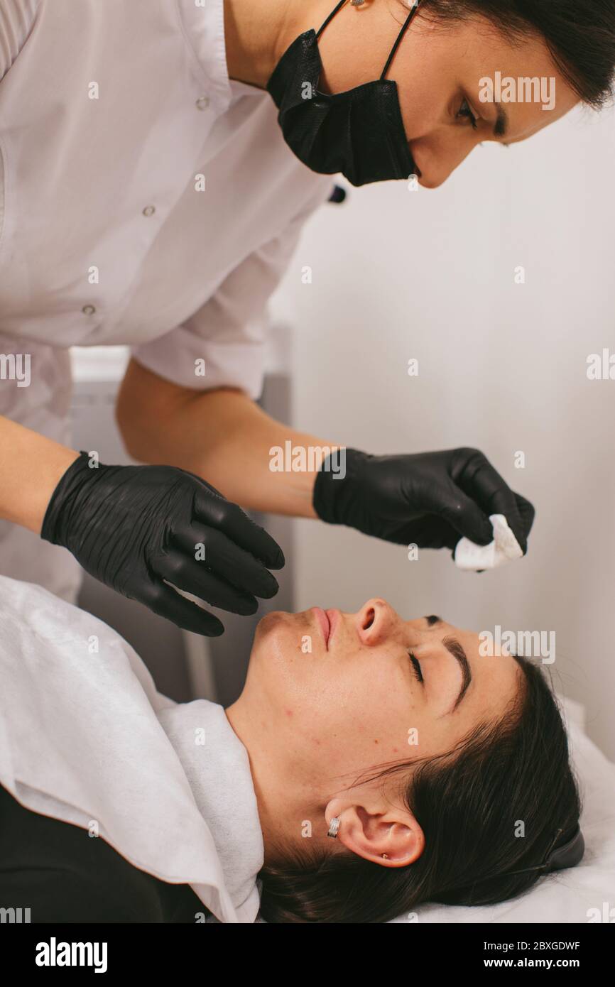 Estetista che pulisce il viso di una donna dopo un trattamento di bellezza con buccia di carbonio Foto Stock