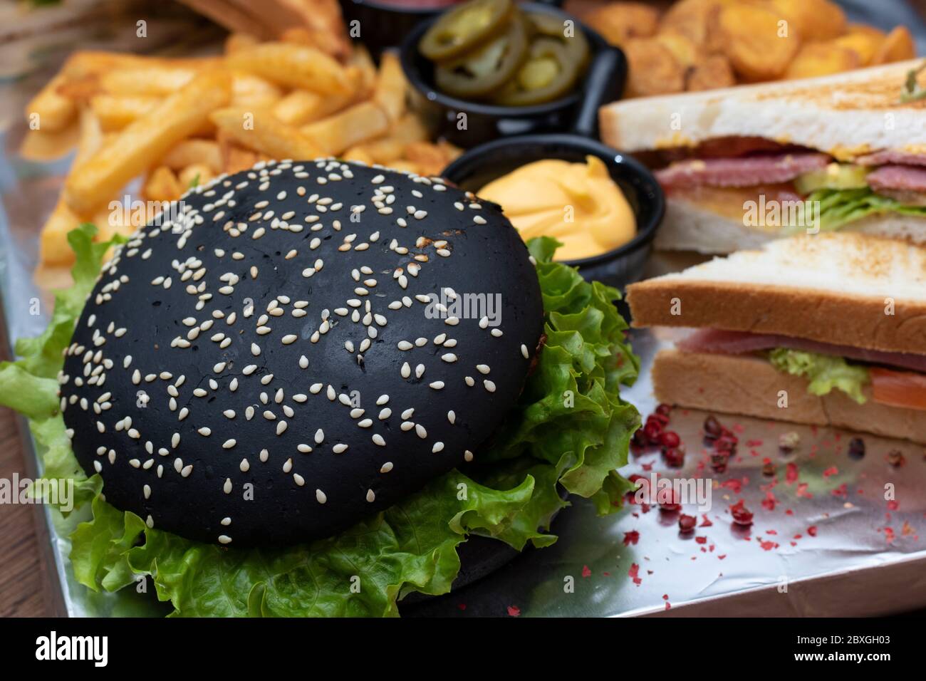 Panini con patate, patatine fritte e hamburger nero con foglie di insalata Foto Stock