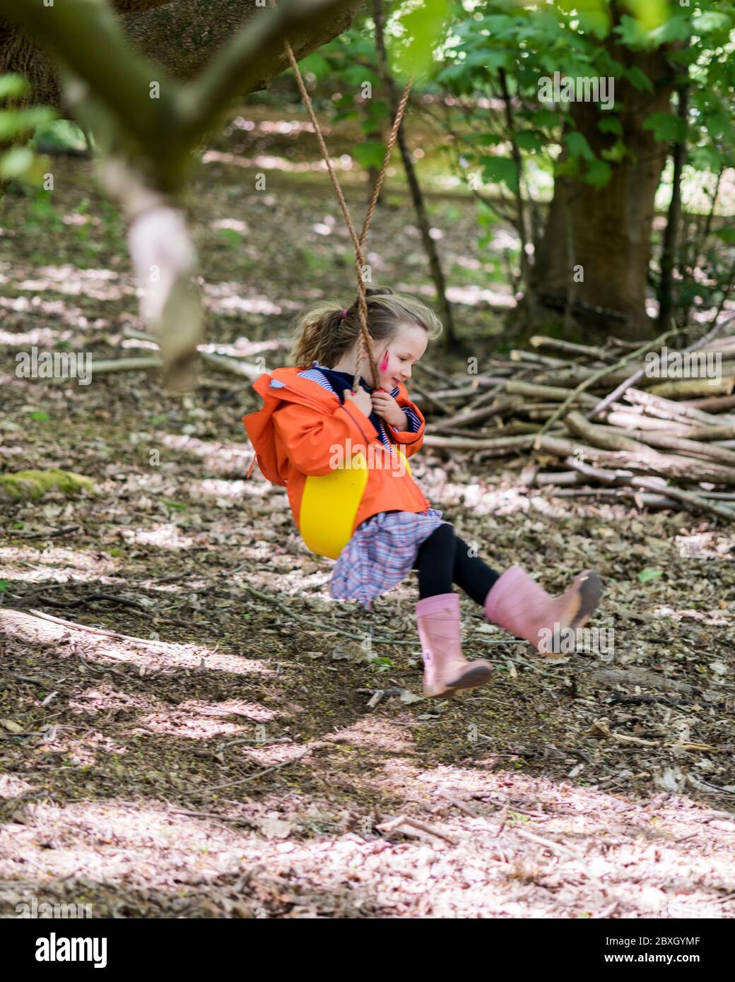 Bambina in arcobaleno arancione che gioca nei boschi in altalena, in den, vicino all'albero Foto Stock