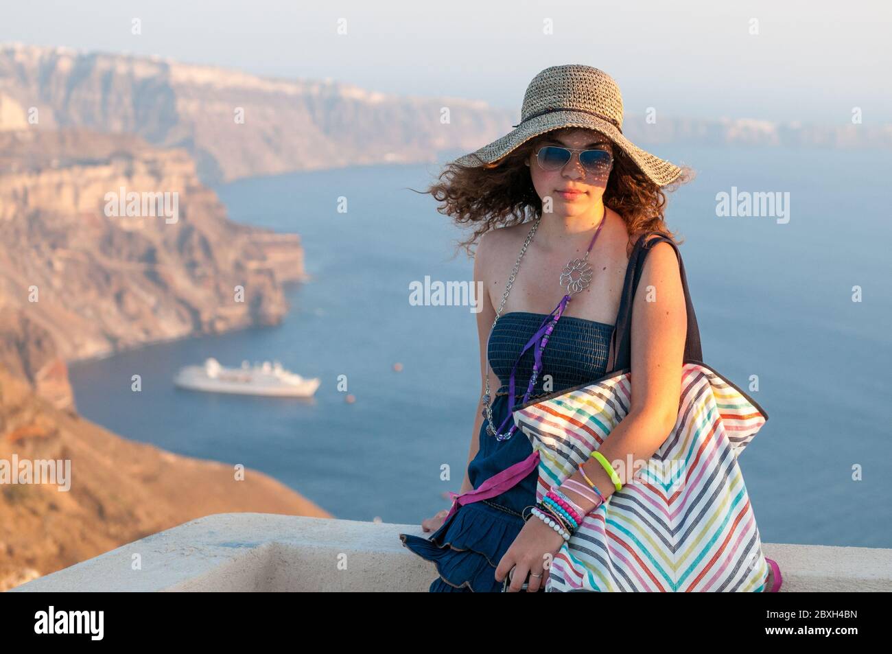 Bella ragazza felice che indossa un cappello con vista caldera dietro a Santorini Island in Grecia. Vacanze estive nelle isole greche Foto Stock