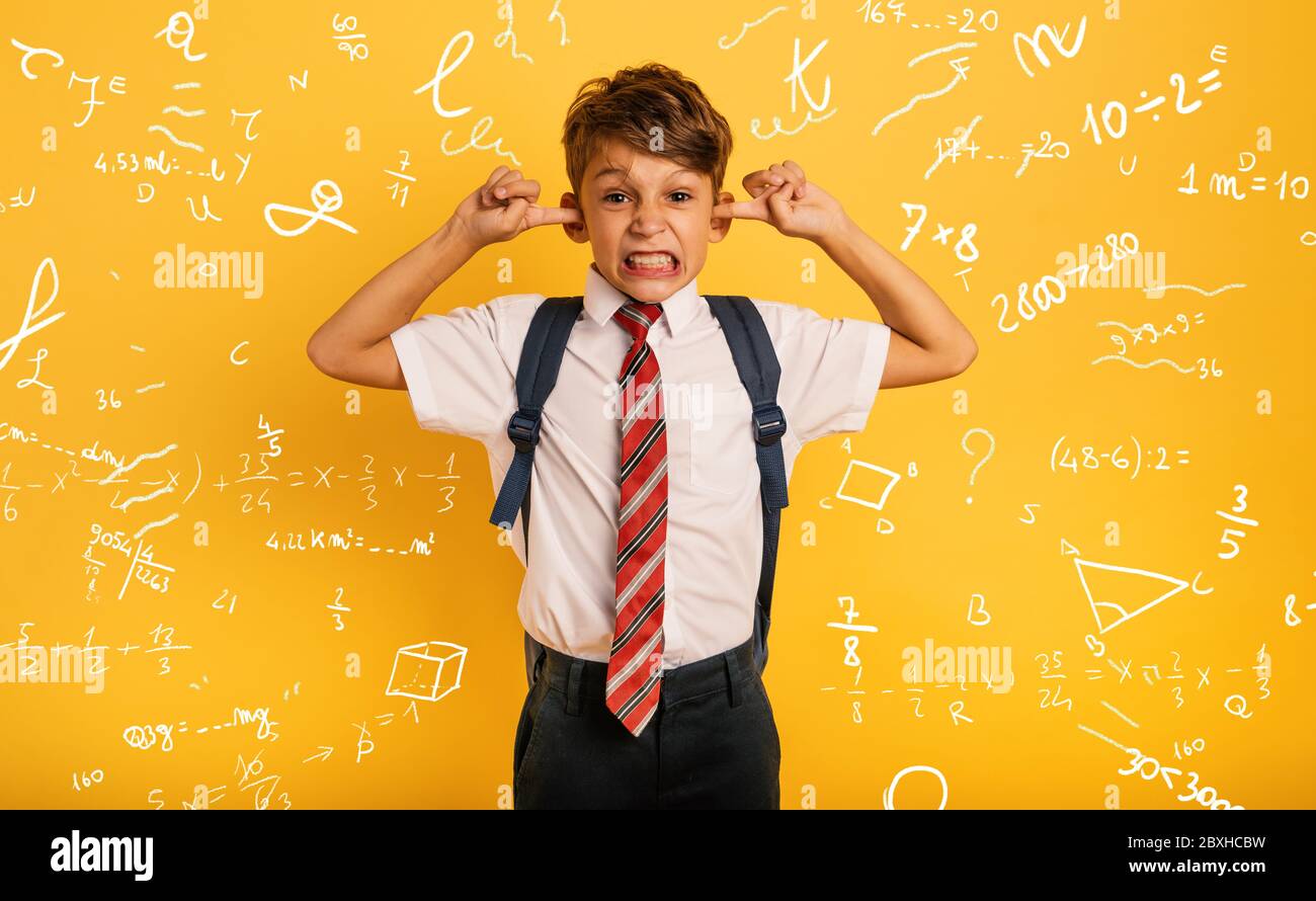 Studente Bambino copre le orecchie perché non vuole sentire il rumore. Sfondo giallo Foto Stock